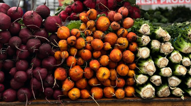 A vibrant display of beets, golden beets, and celery at a farmer's market stall.